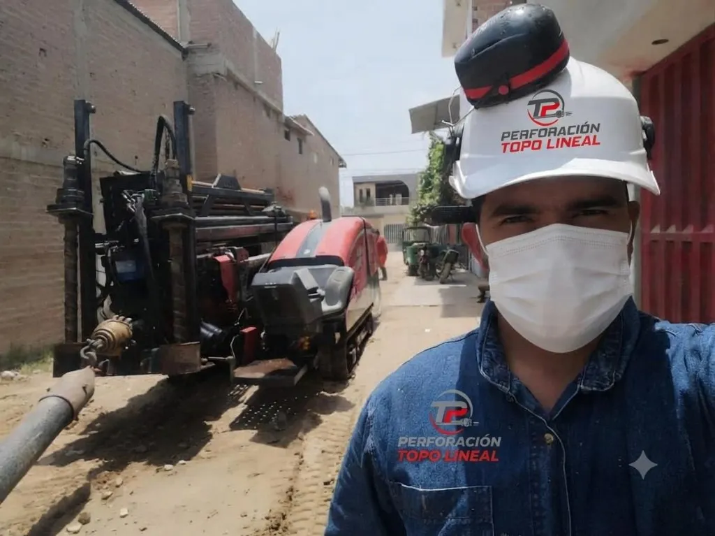 Operario real de Perforación Topo Lineal con casco blanco y máquina perforadora HDD roja operando en calle urbana