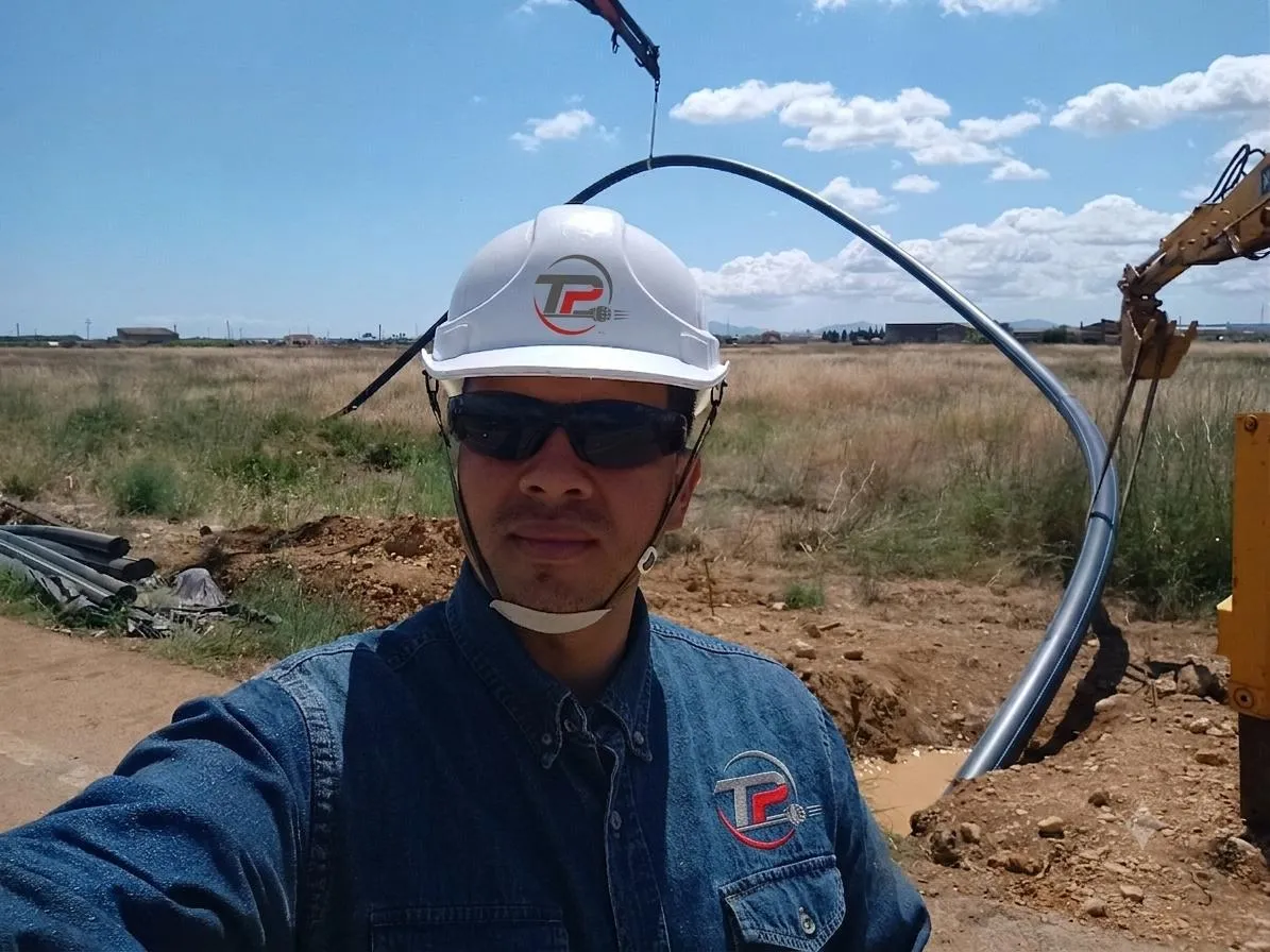 Operario de Perforación Topo Lineal con casco y ropa corporativa junto a tubería de acero curvada izada por grúa para su instalación mediante perforación horizontal